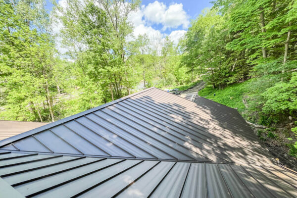 High-angle view of a completed dark bronze residential metal roof surrounded by trees.